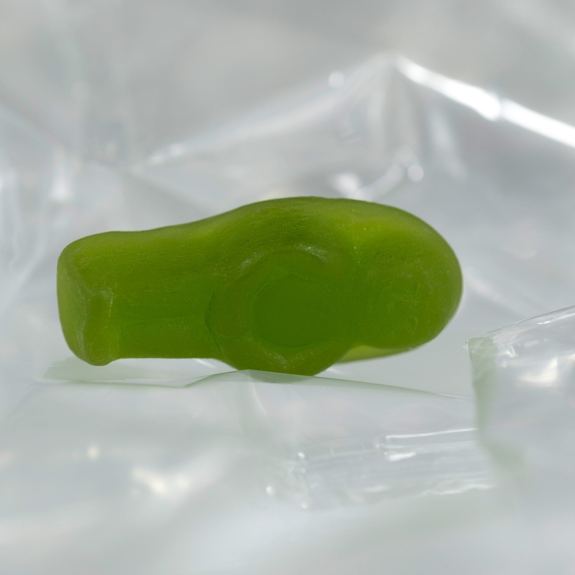 Close-up of a translucent green baby-shaped confectionery figure lying on its side against clear folded material.