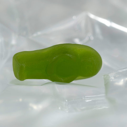 Close-up of a translucent green baby-shaped confectionery figure lying on its side against clear folded material.