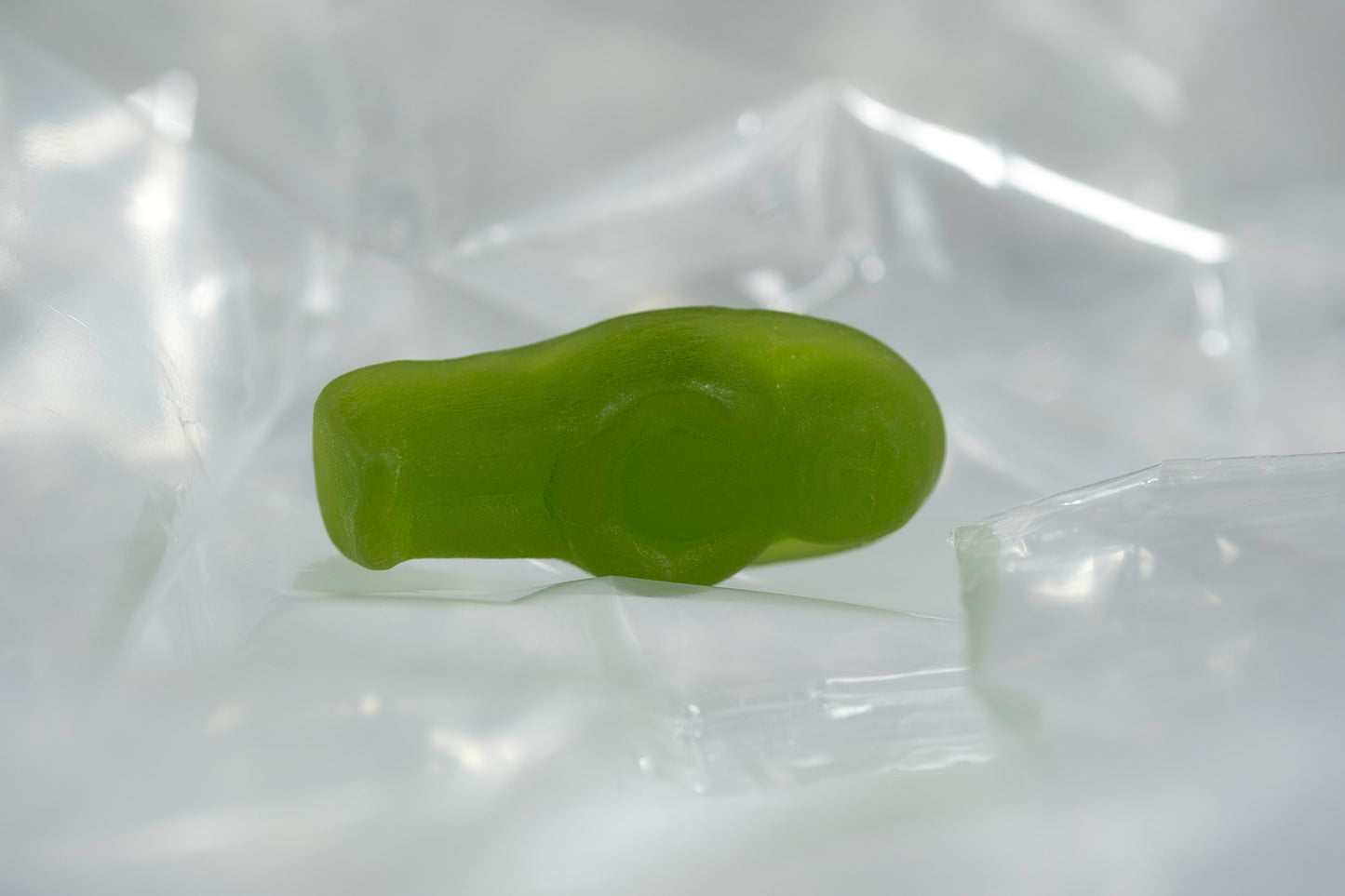 Green translucent baby-shaped figure resting within a softly illuminated field of transparent folded material.