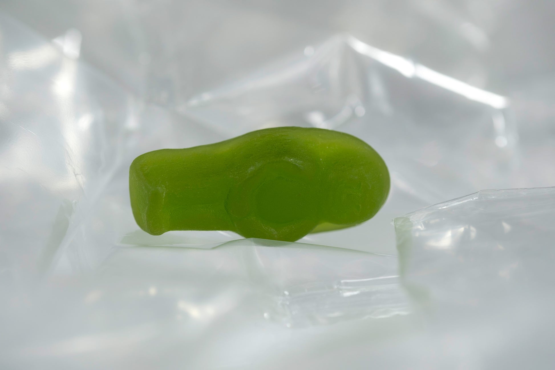 Green translucent baby-shaped figure resting within a softly illuminated field of transparent folded material.