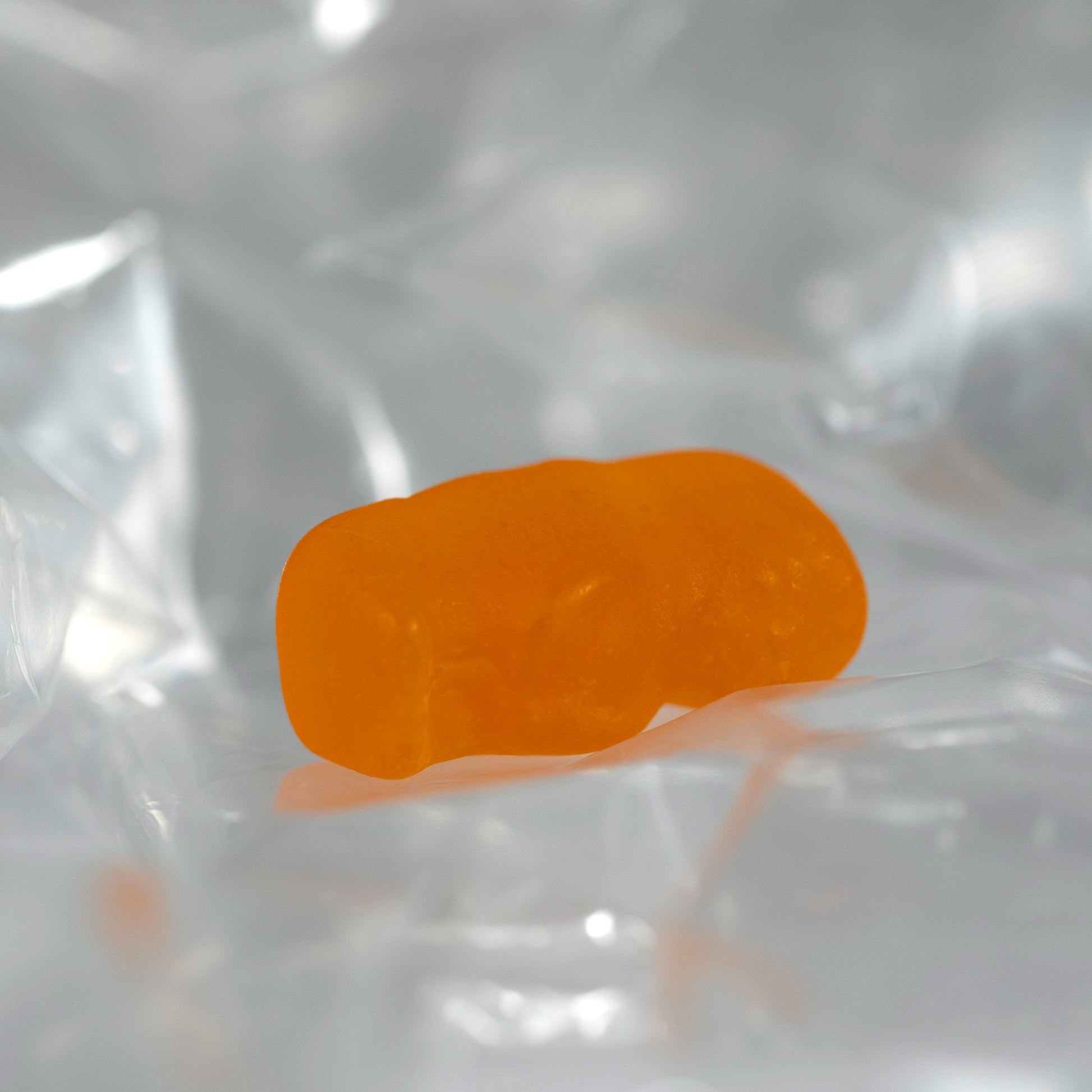 Close-up of a translucent orange baby-shaped confectionery figure lying on its side among pale transparent folds.