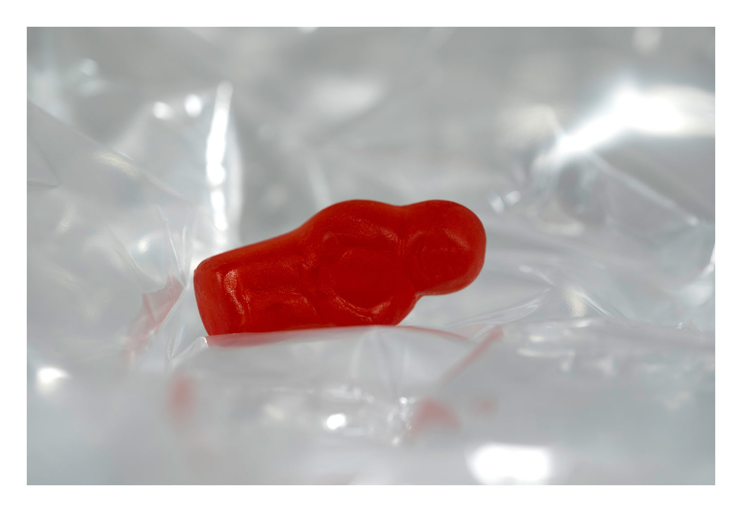 Translucent red baby-shaped figure resting within luminous folds of clear material against a pale silver-white background.