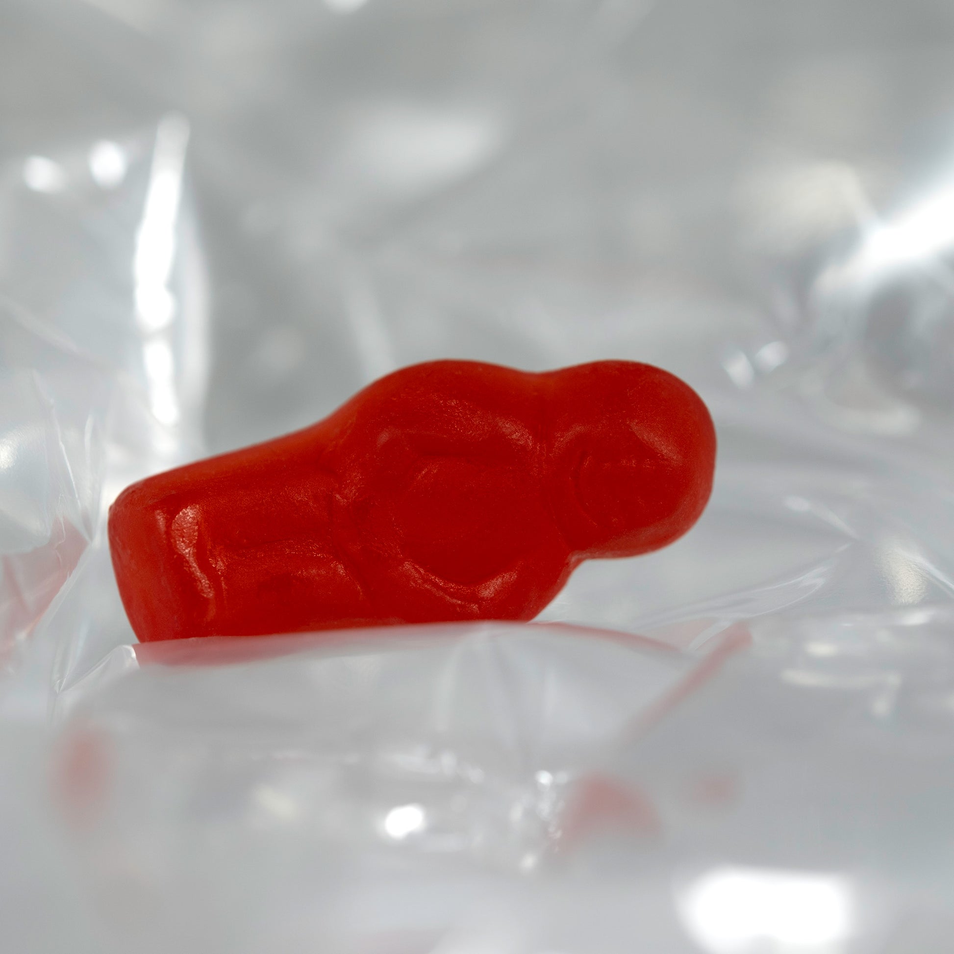 Close-up of a translucent red baby-shaped confectionery figure lying on its side among softly illuminated transparent folds.