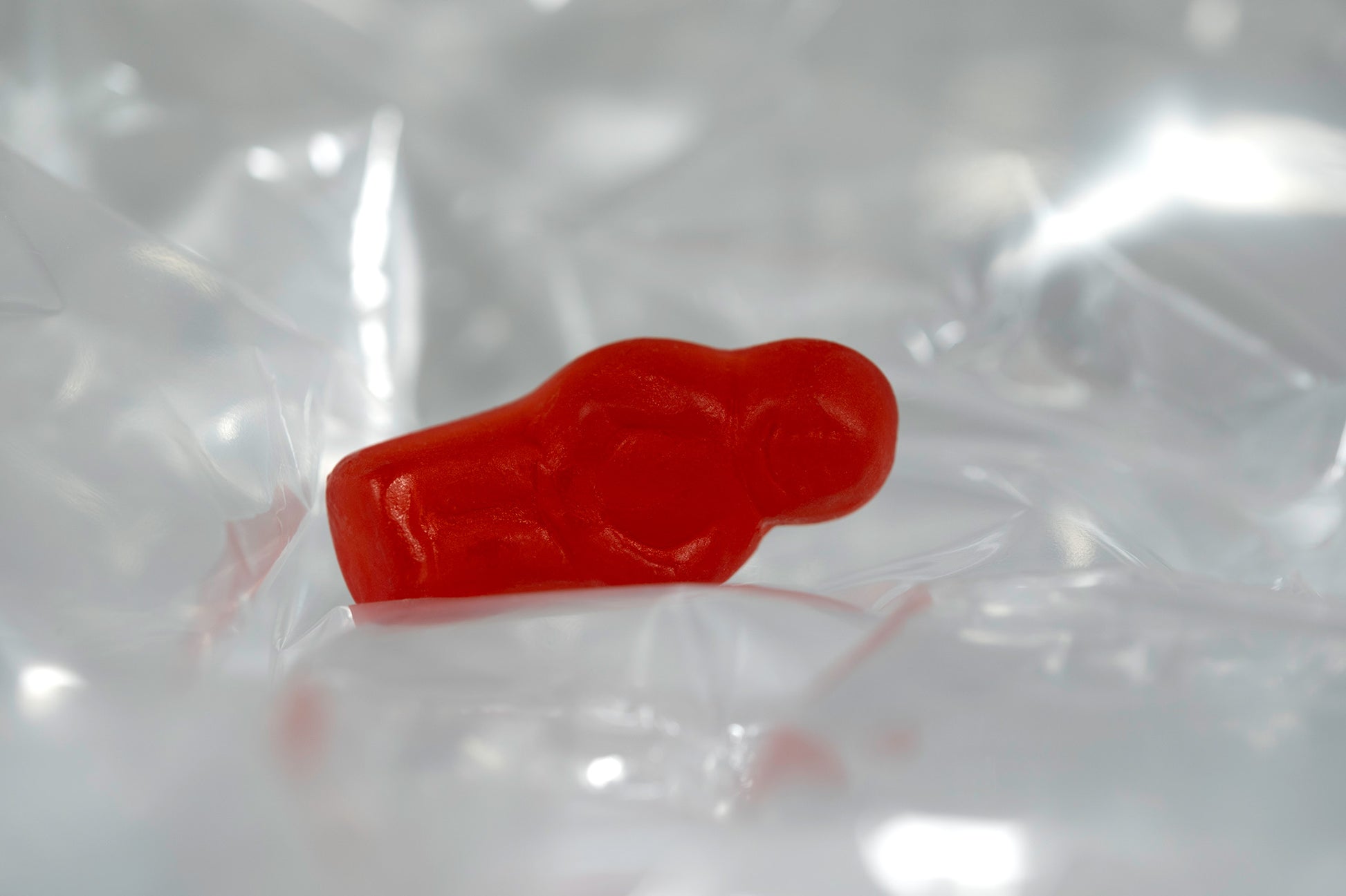 Red translucent baby-shaped figure resting horizontally within reflective transparent material.