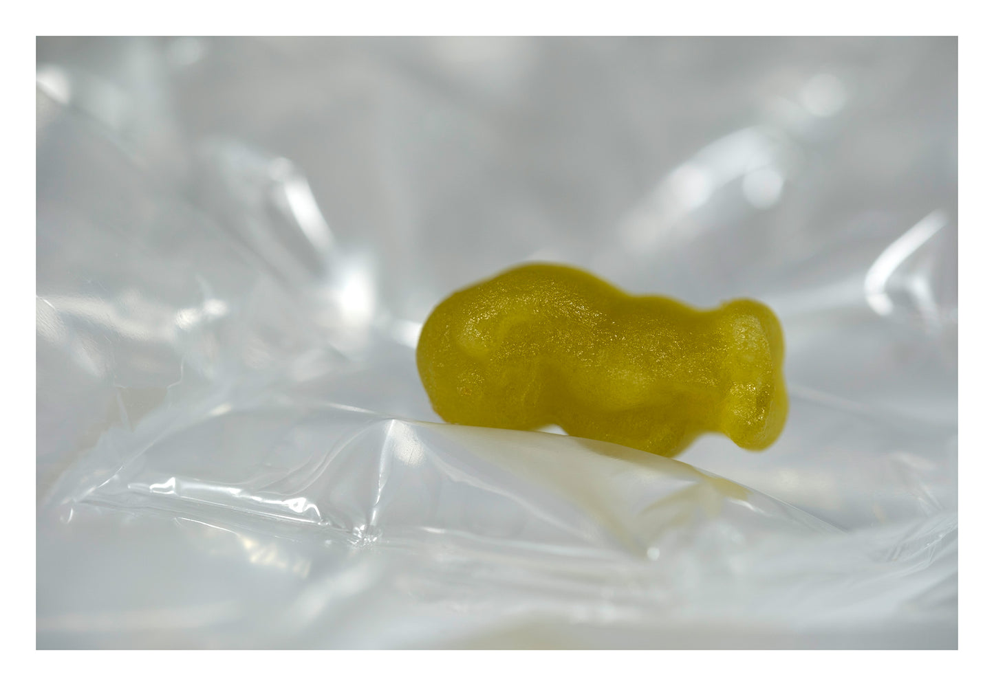 Yellow baby-shaped confectionery figure resting horizontally within luminous folds of transparent material.