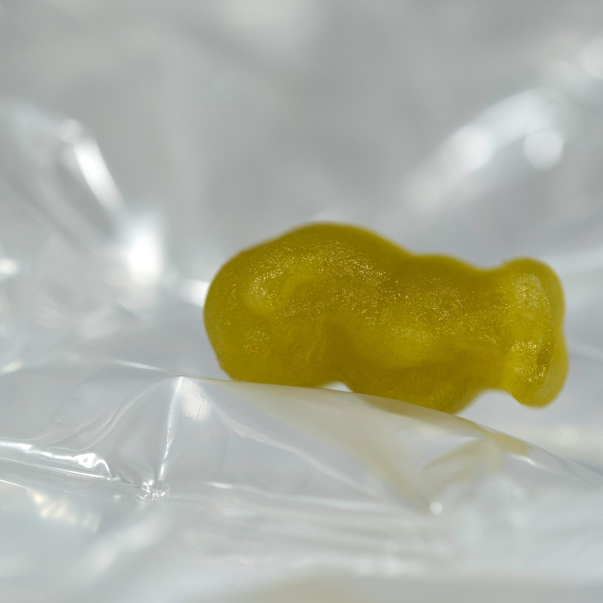 Close-up of a translucent yellow baby-shaped figure curled on its side among softly illuminated transparent folds.