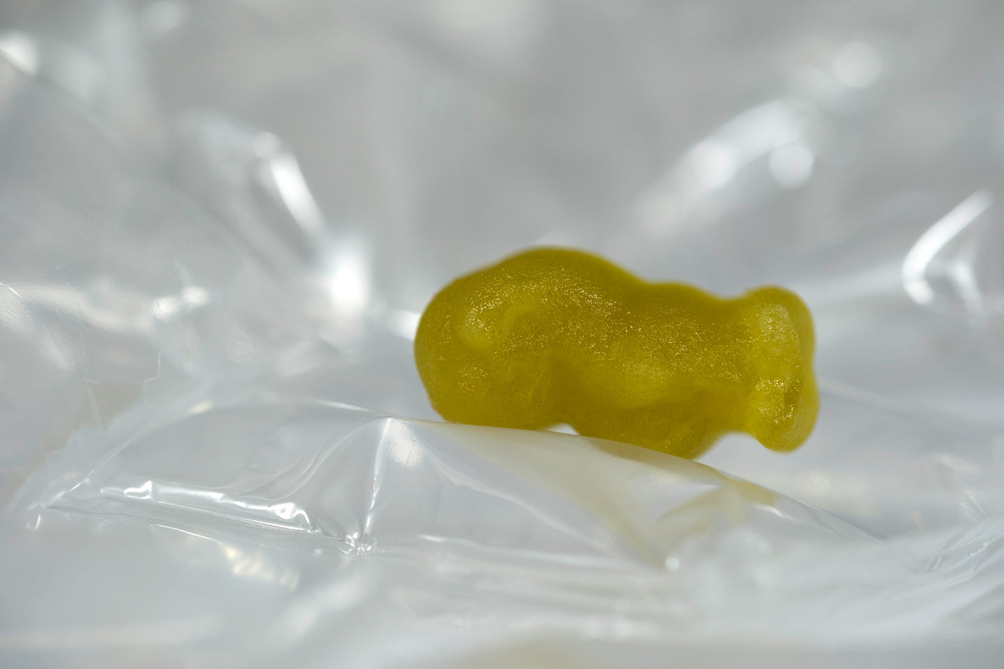 Yellow baby-shaped figure resting on folded transparent material against a soft silver-white background.