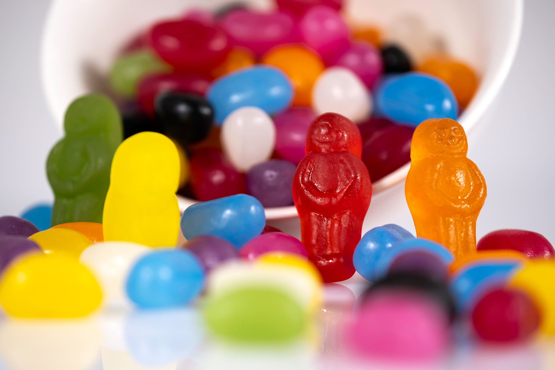 Green, yellow, red and orange jelly baby figures stand among colourful spilled jelly beans in Spill the Beans - 266468v1.
