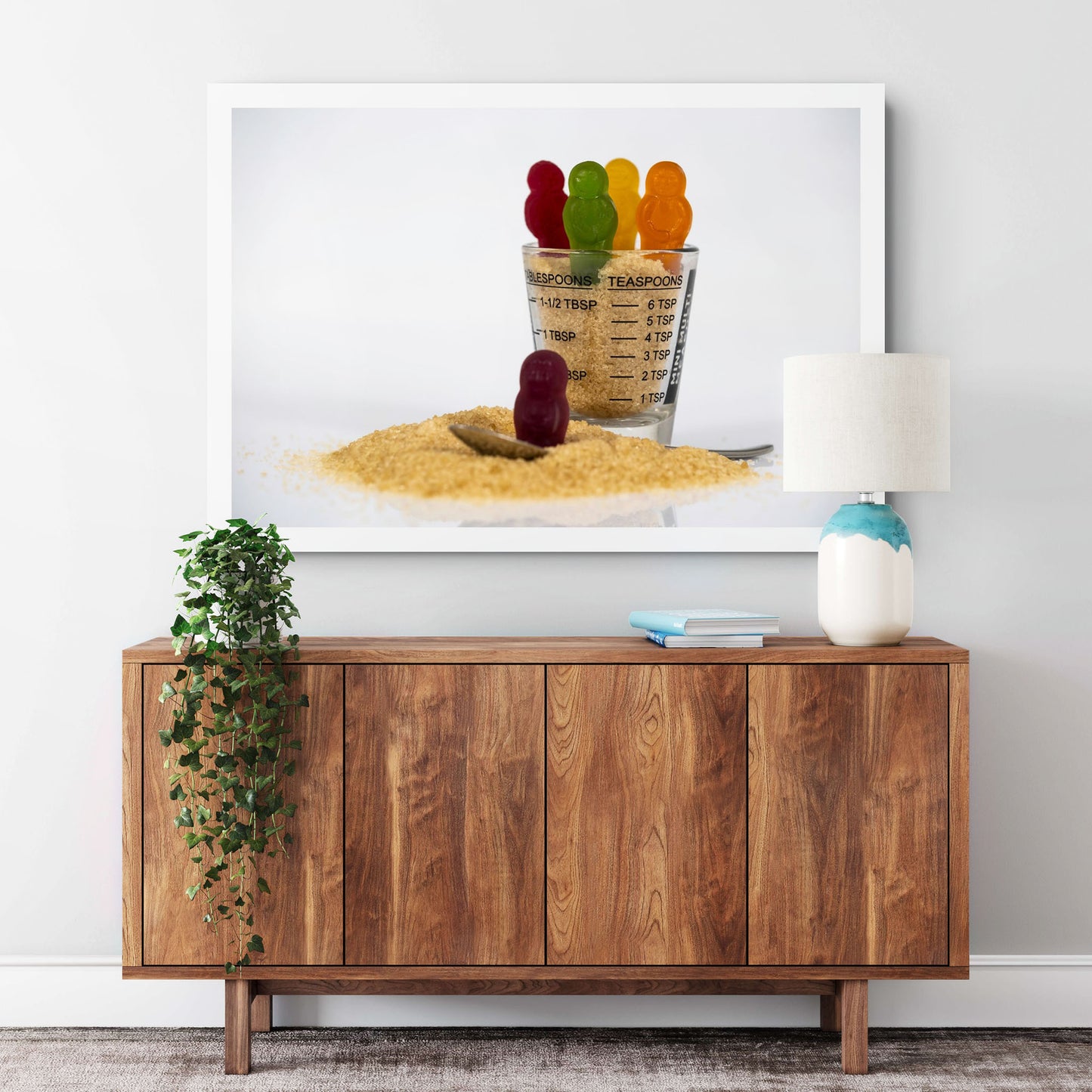 Spoonful Of Sugar - 267000v1 framed photographic artwork featuring colourful confectionery figures, raw sugar, a measuring glass and teaspoon displayed in a contemporary interior.