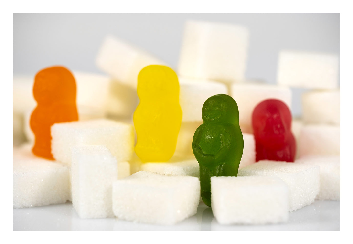 Four colourful confectionery figures in orange, yellow, green and red stand among scattered white sugar cubes in Sugar Babies - 266997v1.