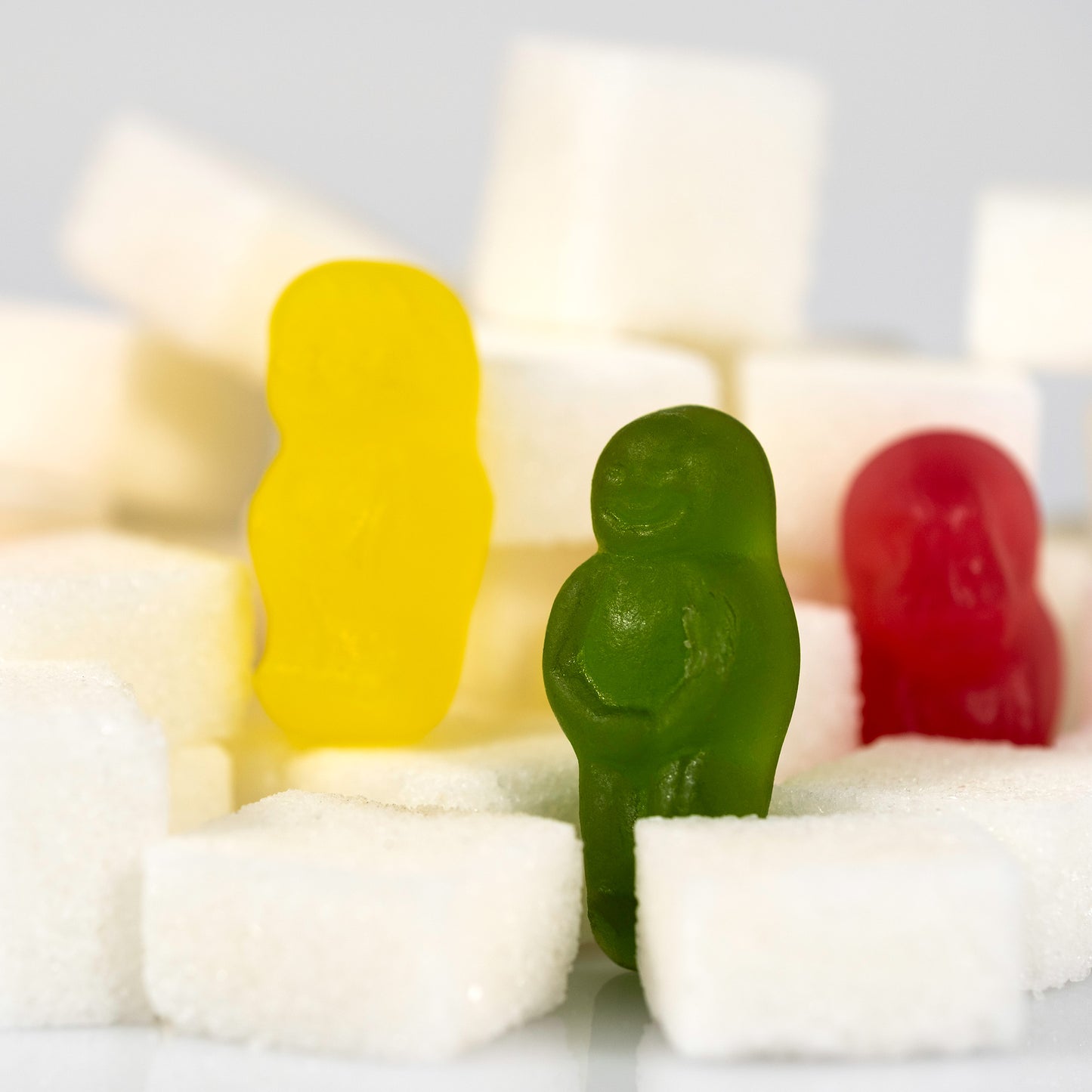Green, yellow and red confectionery figures emerge between oversized white sugar cubes in a close crop of Sugar Babies - 266997v1.