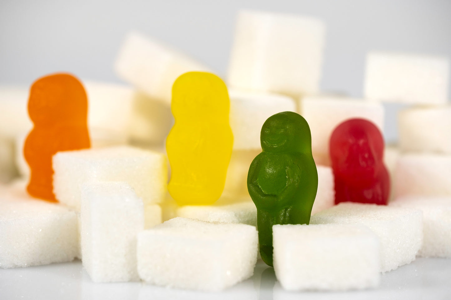 Four colourful confectionery figures stand among scattered white sugar cubes, creating a miniature geometric landscape in Sugar Babies - 266997v1.