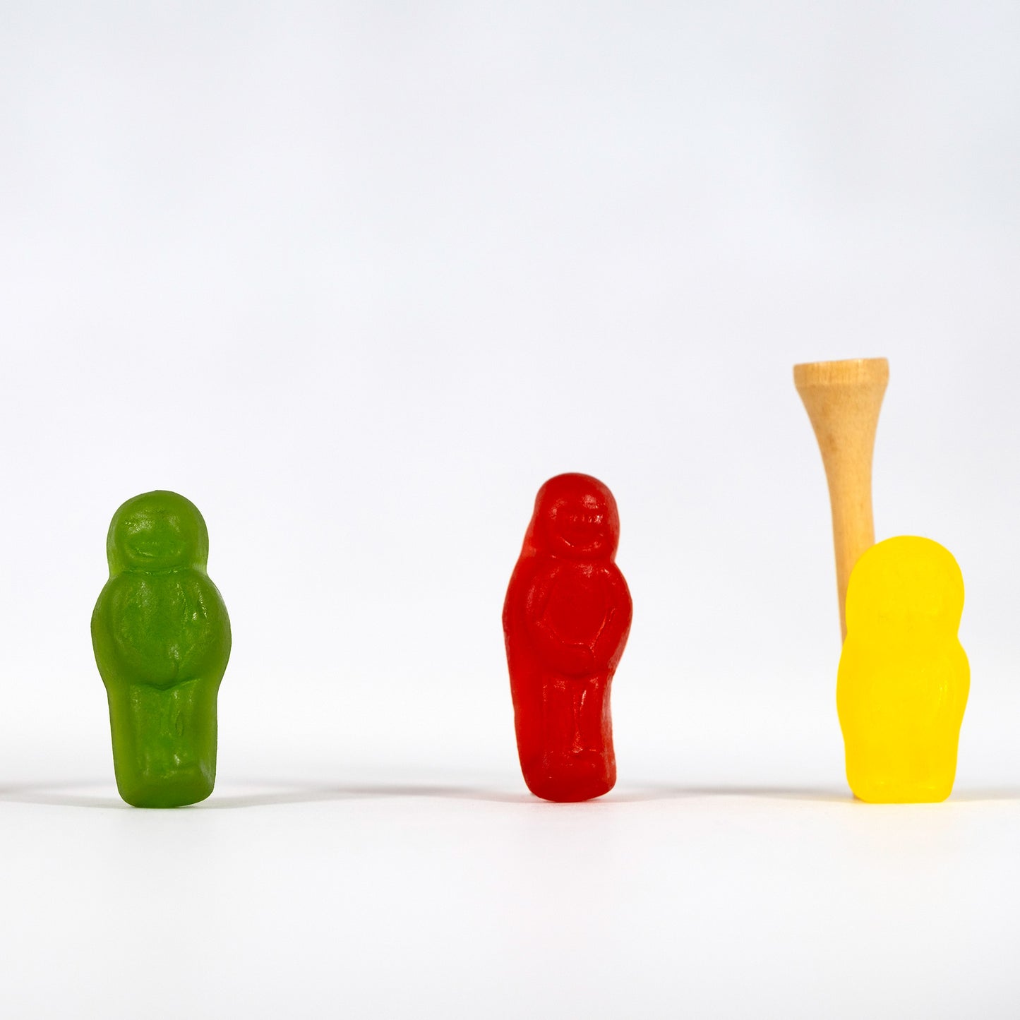 Green, red and yellow confectionery figures stand widely spaced against a white background, with a wooden golf tee rising behind the yellow figure in Teeing Off - 267089v1.