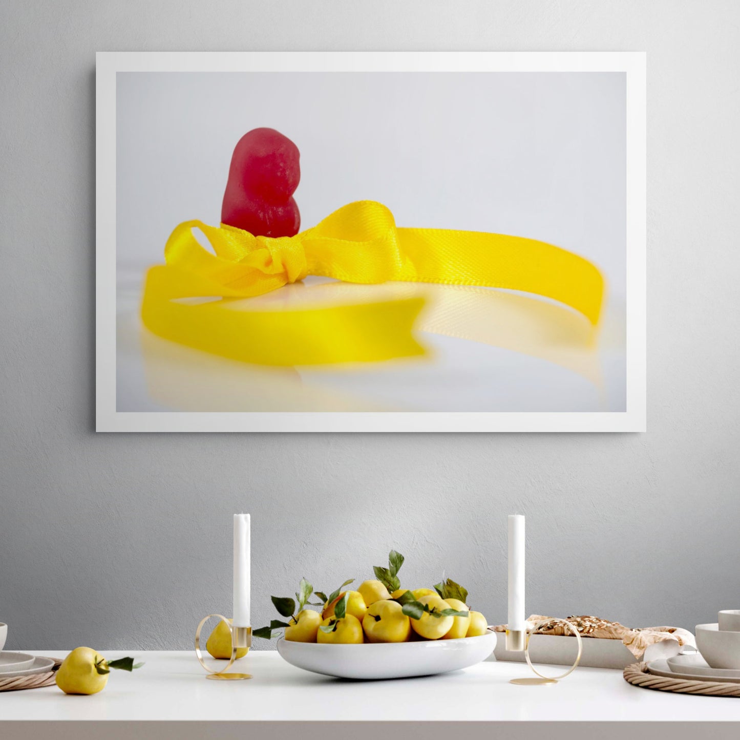 Tie A Yellow Ribbon - 267070v1 framed photographic artwork featuring a red confectionery figure behind a bright yellow satin ribbon tied in a bow, displayed in a contemporary interior.