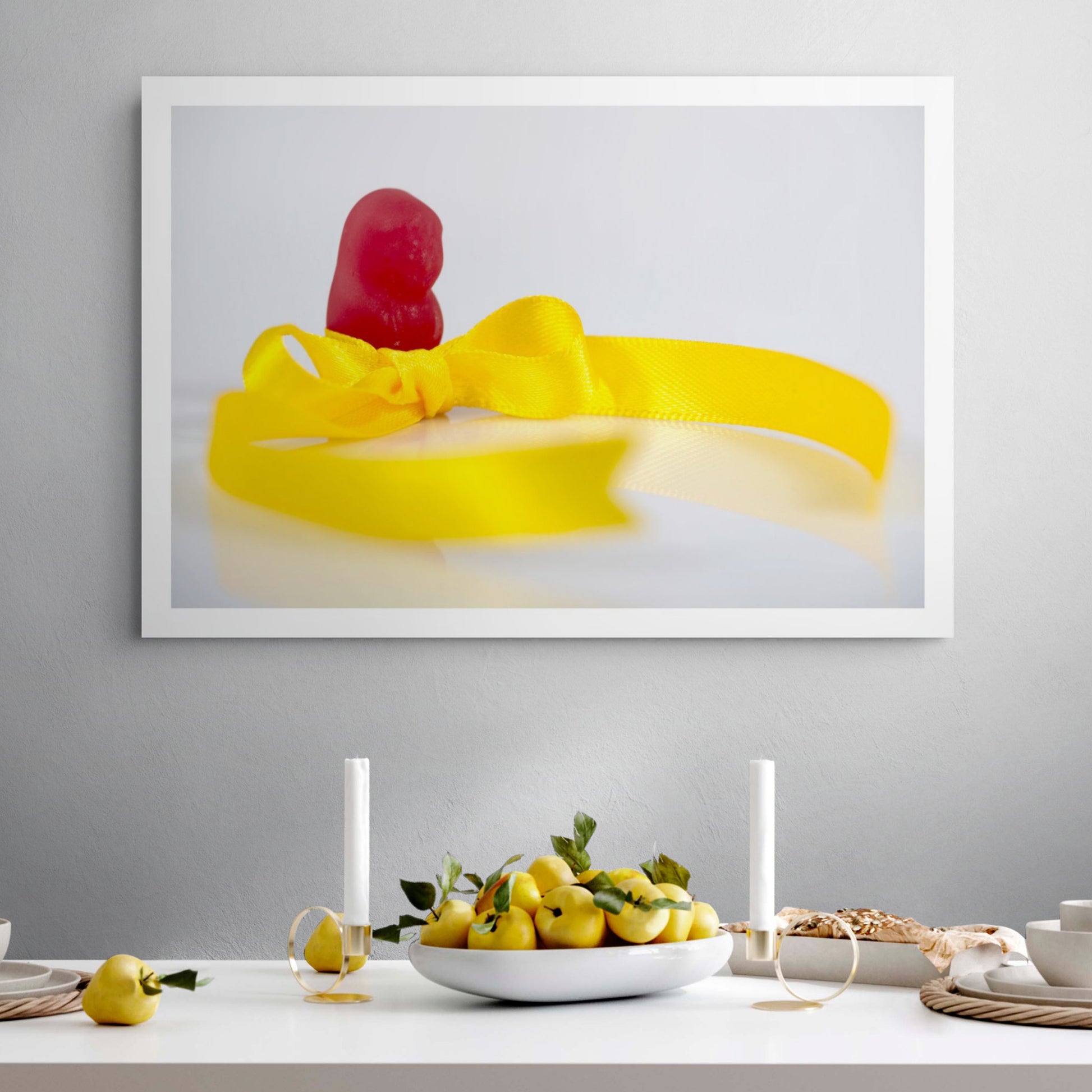 Tie A Yellow Ribbon - 267070v1 framed photographic artwork featuring a red confectionery figure behind a bright yellow satin ribbon tied in a bow, displayed in a contemporary interior.