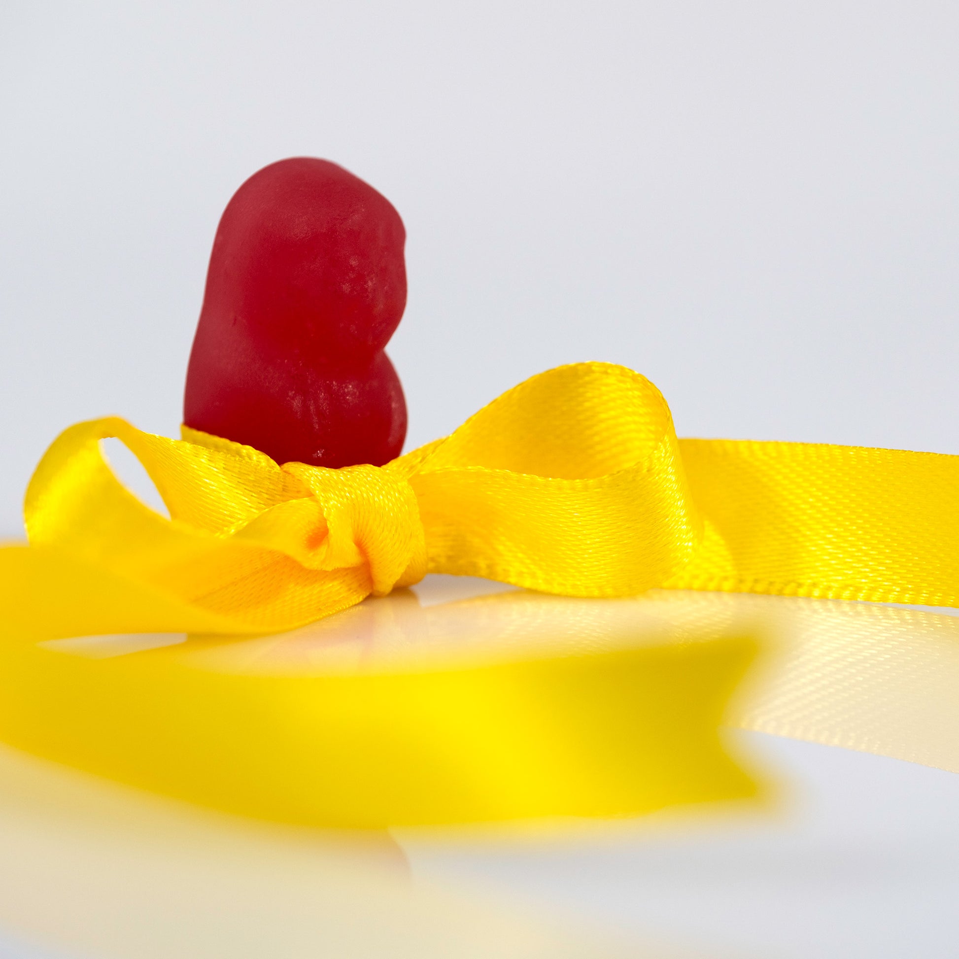 Close view of a red confectionery figure rising behind a bright yellow satin bow with sweeping loops of ribbon in Tie A Yellow Ribbon - 267070v1.