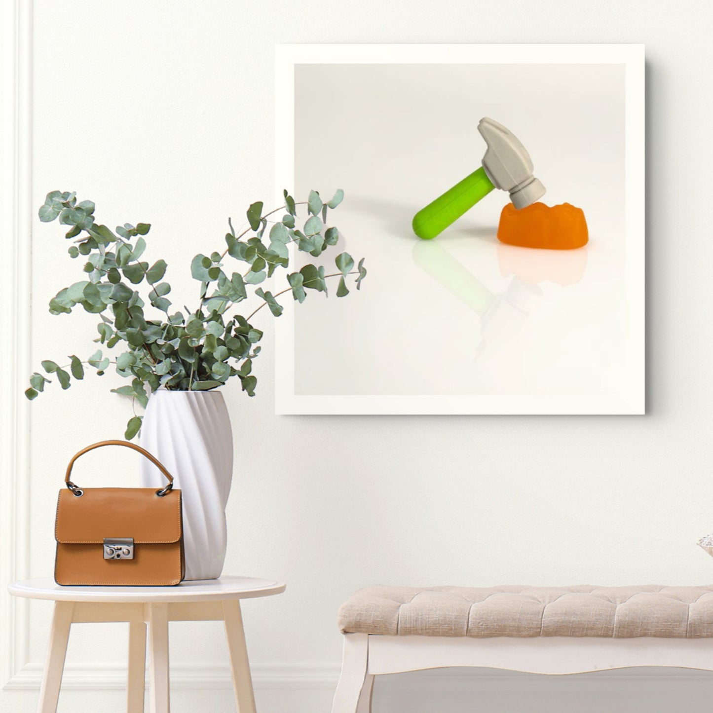 Under The Hammer - 266707v2 framed photographic artwork featuring a miniature hammer with a green handle poised above an orange confectionery form, displayed in a contemporary interior.