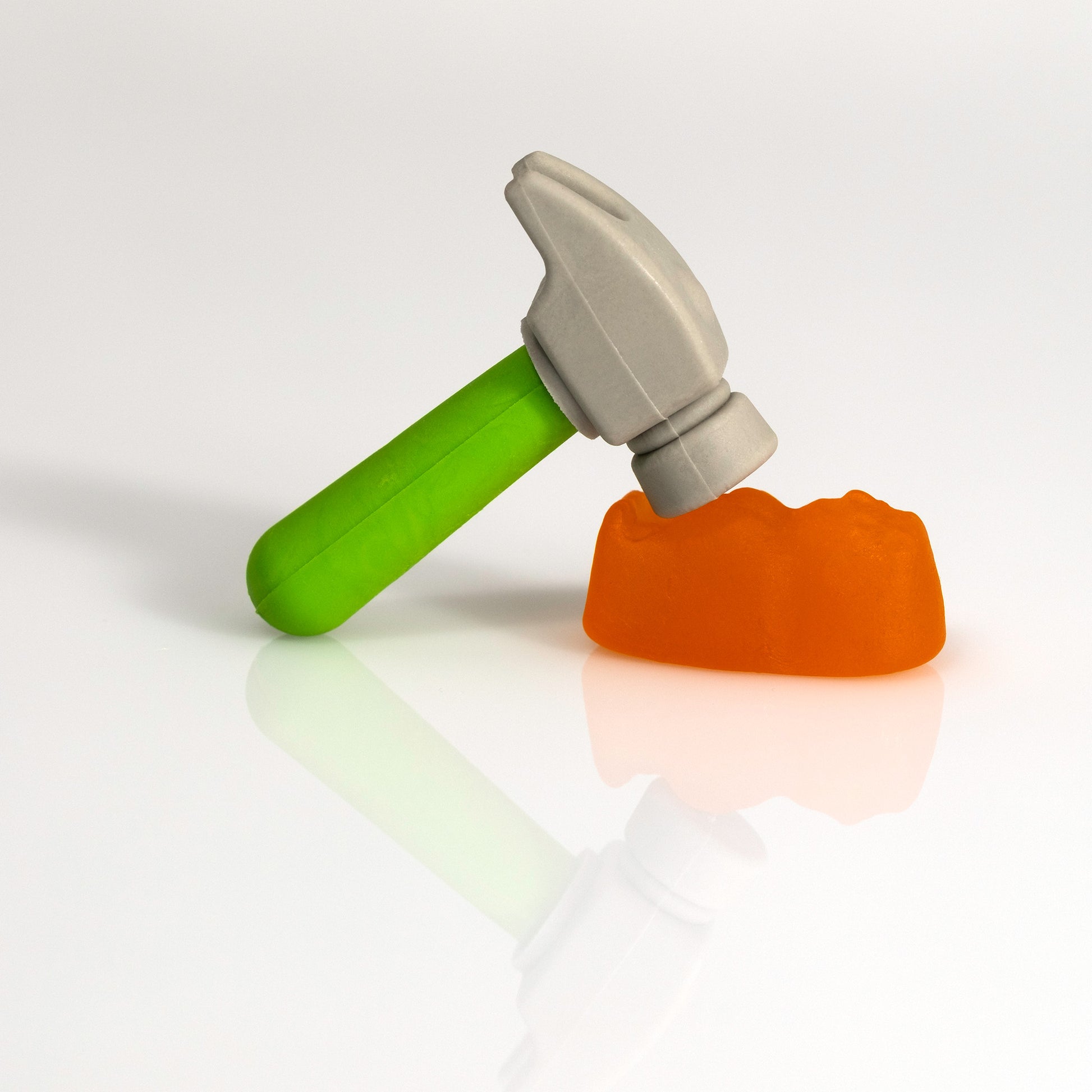 Close view of a miniature grey hammer with a bright green handle poised over an orange confectionery form in Under The Hammer - 266707v2.