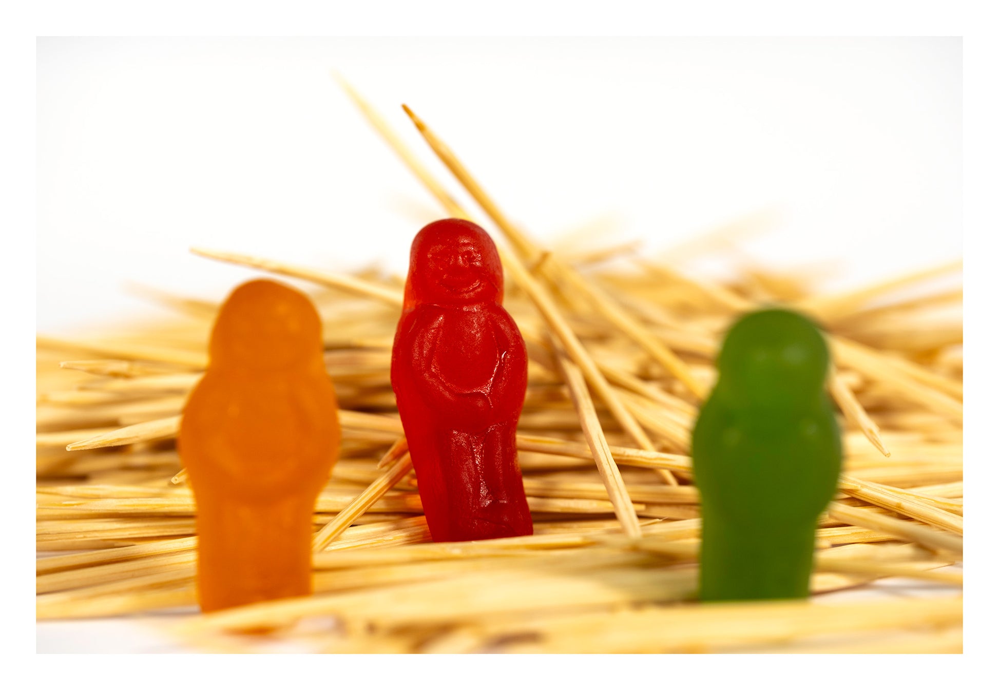 Red confectionery figure in sharp focus between blurred orange and green figures within a chaotic field of wooden toothpicks in What A Pick - 267283v1.
