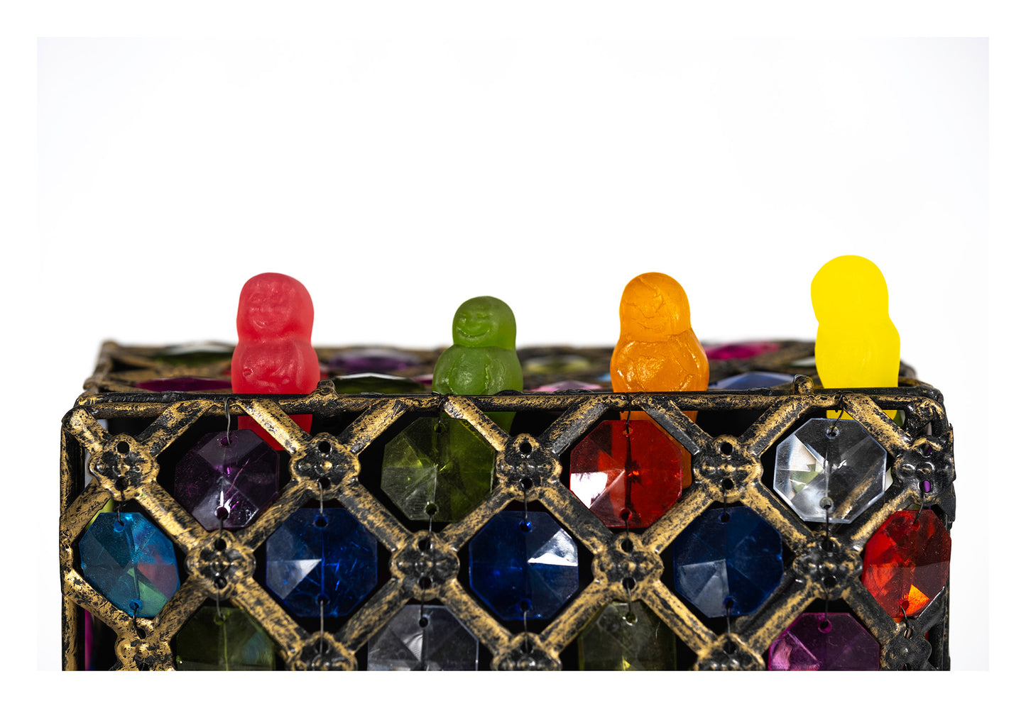 Four red, green, orange and yellow confectionery figures standing above an ornate gold lattice decorated with colourful jewel-like facets.