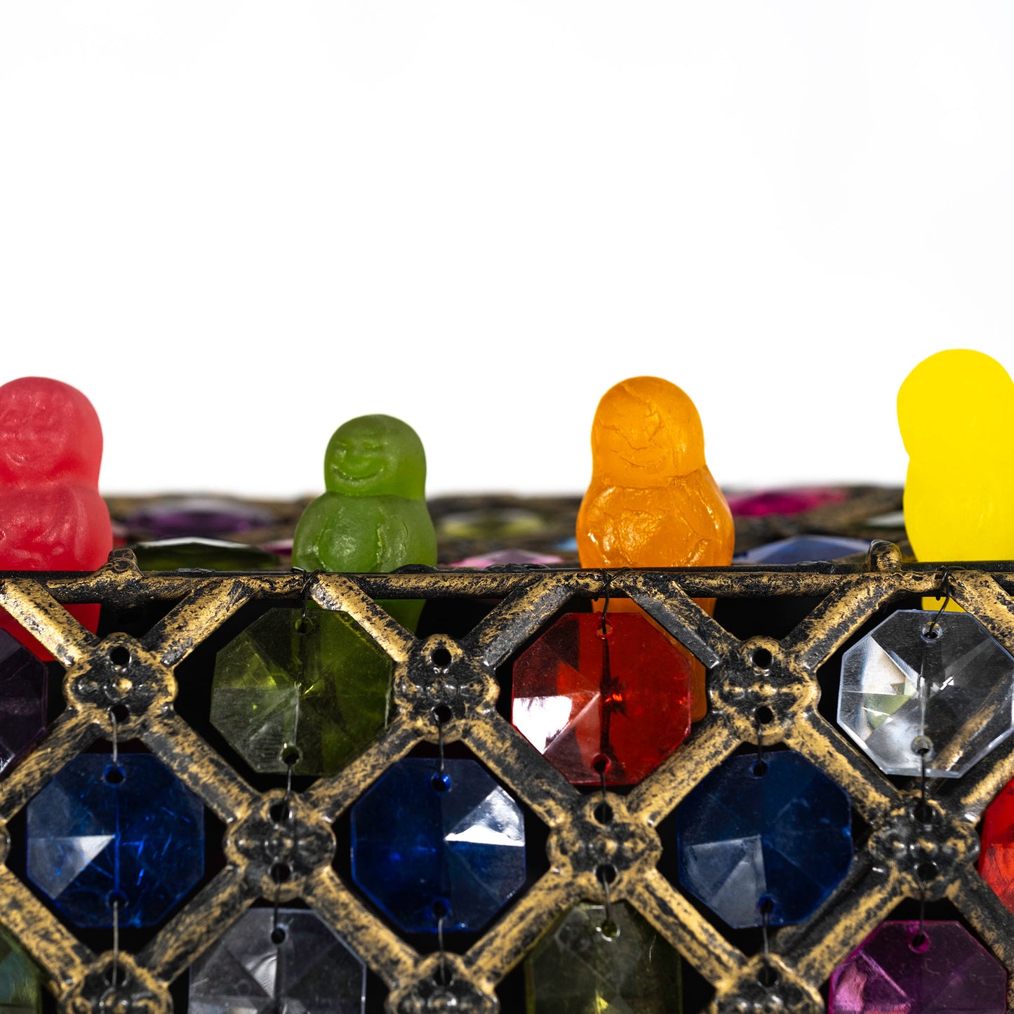 Close square crop of four colourful confectionery figures above a distressed gold lattice filled with red, blue, green and purple jewel-like facets.