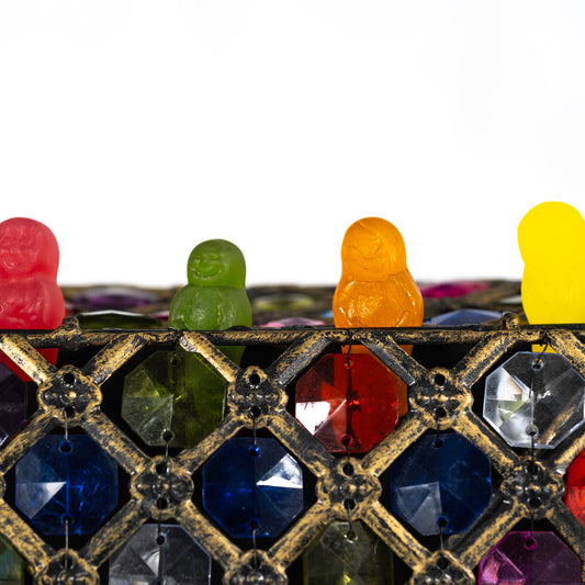 Close square crop of four colourful confectionery figures above a distressed gold lattice filled with red, blue, green and purple jewel-like facets.