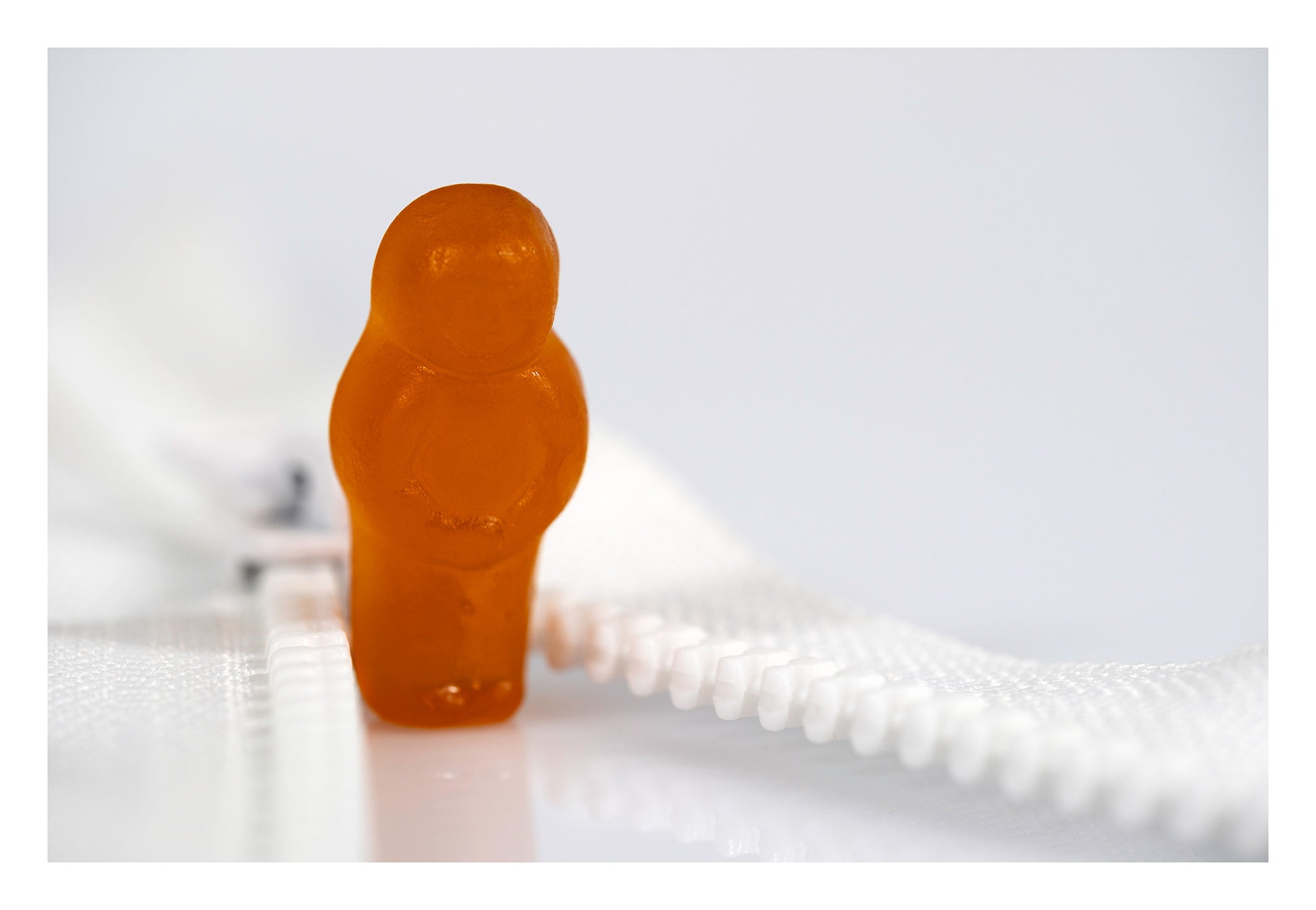 Orange confectionery figure standing at the opening of a white zip against a minimalist white background.