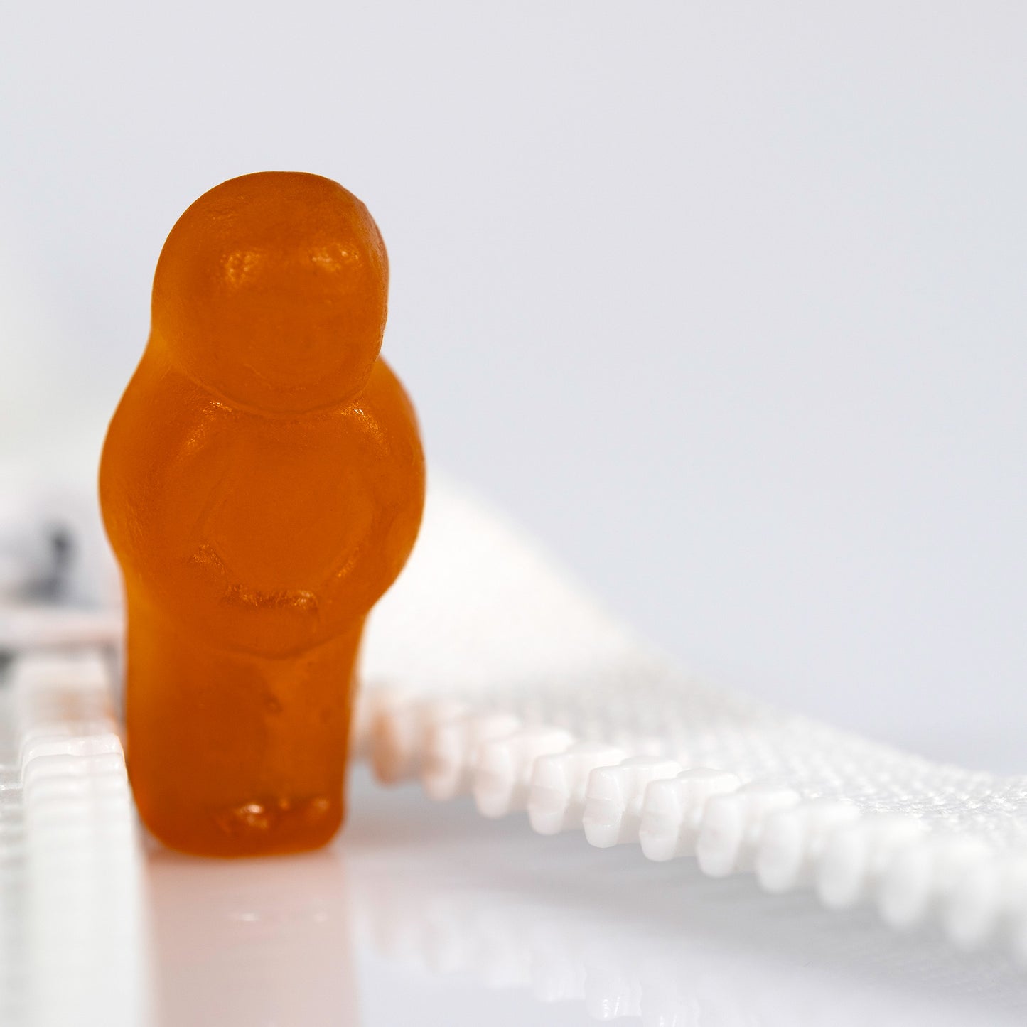 Close crop of an orange confectionery figure beside the white teeth of an open zip with expansive white negative space.