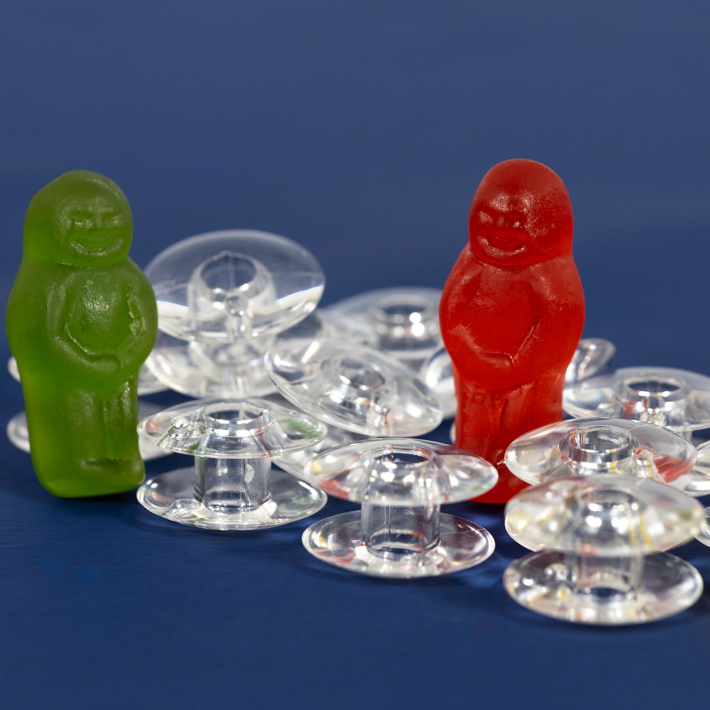 Green and red jelly baby figurines surrounded by transparent sewing machine bobbins against a deep blue background.