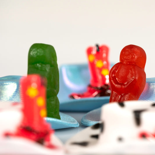 Close view of Boot Scootin Baby showing green and red jelly baby figurines with miniature blue cowboy hats and red boots, ART1.