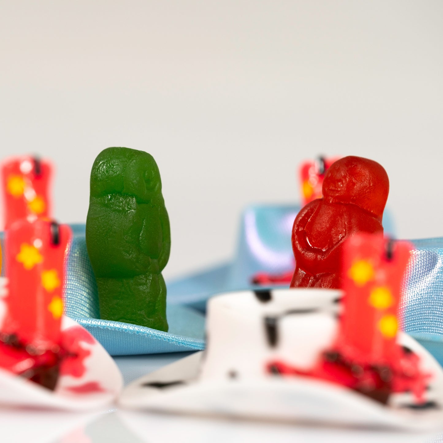 Close view of Boot Scootin Baby showing green and red jelly baby figurines behind miniature cowboy boots and blue hats, ART1.