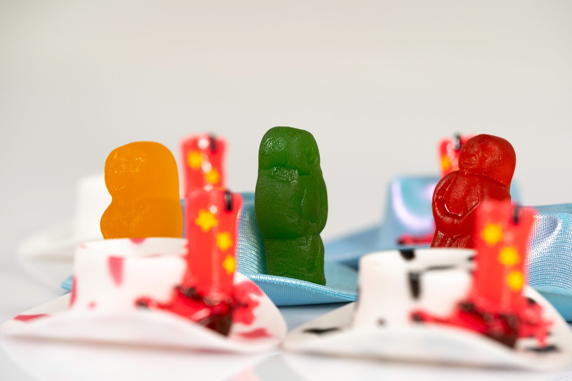 Boot Scootin Baby by Australian photographer Raymond Mather, orange, green and red jelly baby figurines among miniature cowboy hats and boots, ART1.