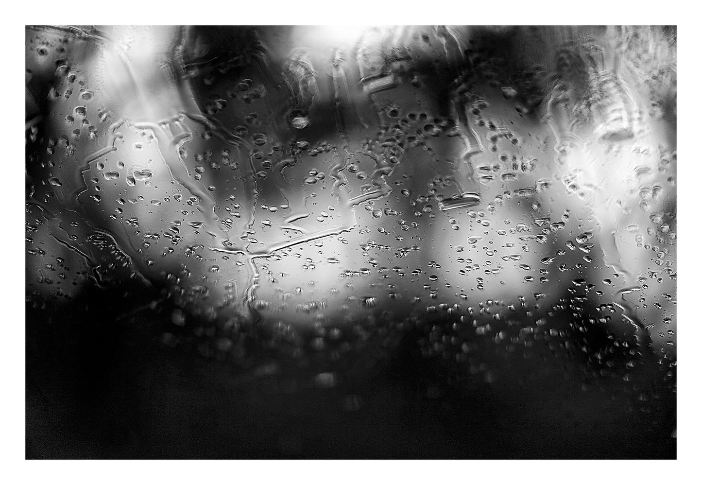 Coastal-Noir 8147 - 104x74cm, black and white coastal photograph with rain-speckled glass creating soft abstract textures over blurred landscape.
