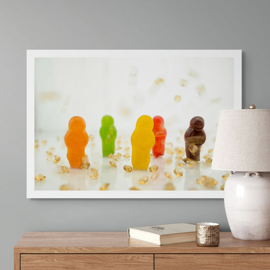 All that Glitters 2871v2 - Room View, colourful jelly baby figurines in orange, green, yellow, red, and purple standing upright among scattered golden crystal fragments on a glossy white surface; playful, pop-art style fine art print by Raymond Mather, ART1.