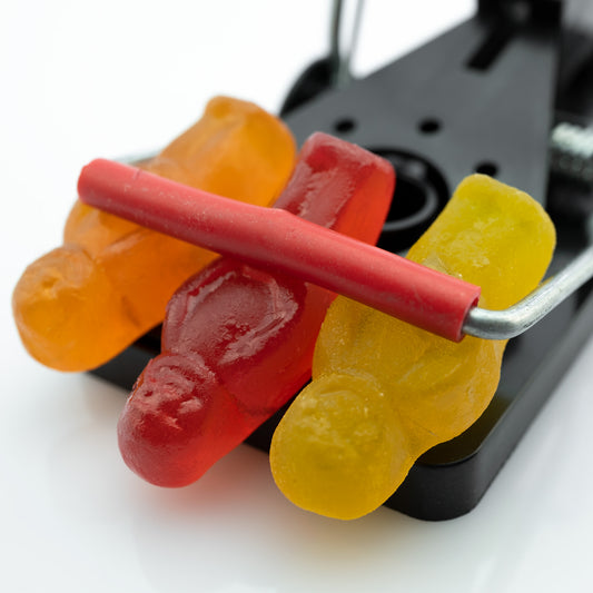 Caught in a Trap 3027 - Close Detail View, fine art photograph of three gummy jelly figures caught beneath the bar of a black metal trap, captured with precision and pop-art wit by Raymond Mather, ART1.