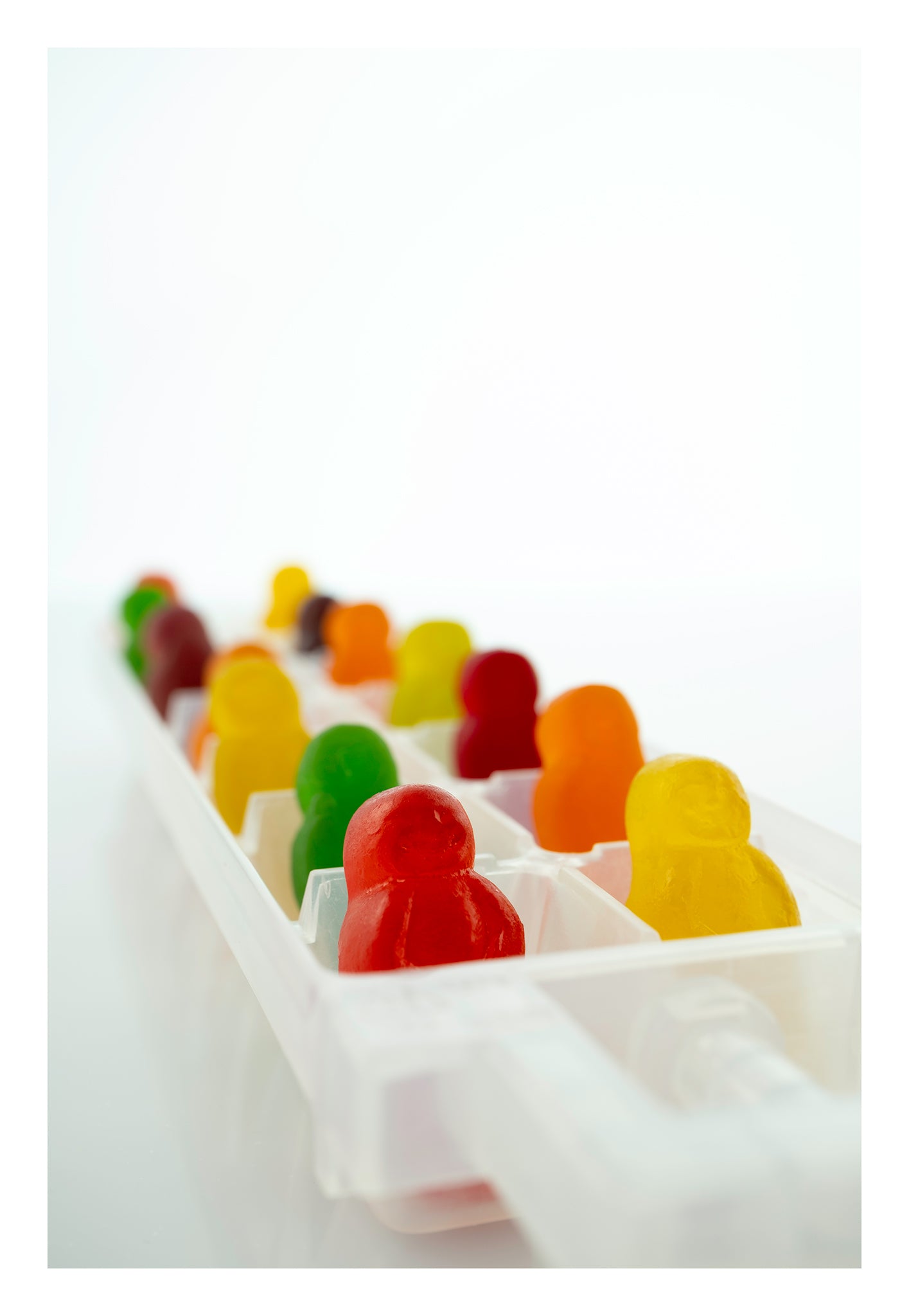 Cold As Ice 2731v1 - 74x104cm, colourful jelly baby figures arranged upright in a white ice cube tray, set against a bright minimalist background, fine art photograph by Raymond Mather, ART1.