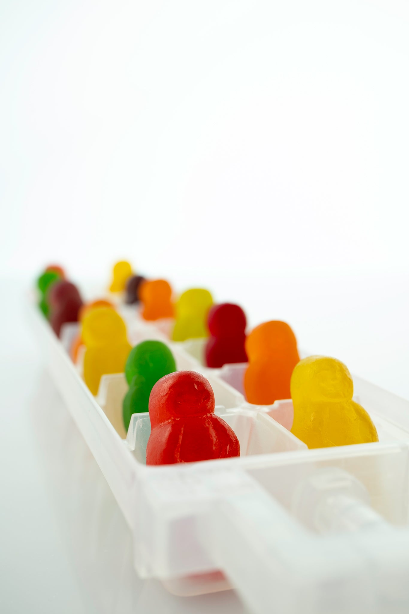 Cold As Ice 2731v1 - 60x90cm, colourful jelly baby figures arranged upright in a white ice cube tray, set against a bright minimalist background, fine art photograph by Raymond Mather, ART1.