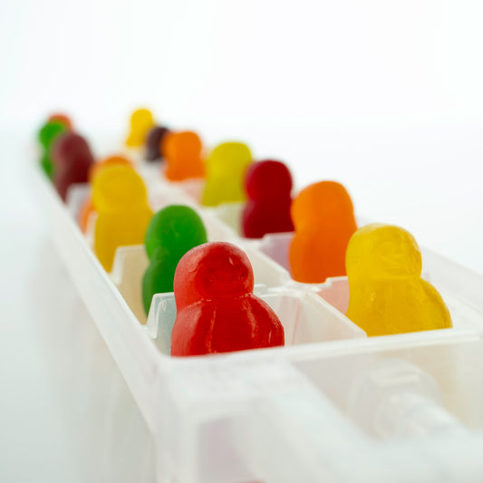 Cold As Ice 2731v1 - Close Detail View, colourful jelly baby figures arranged upright in a white ice cube tray, set against a bright minimalist background, fine art photograph by Raymond Mather, ART1.