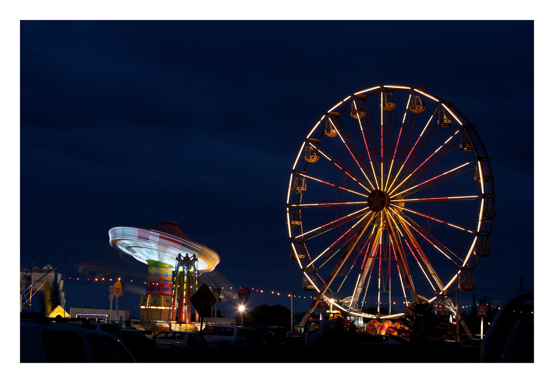 Fairground Carnival Lights 6900003v3 - 104x74cm, Ferris wheel glowing against twilight sky with carnival rides below, fine art limited edition print by Raymond Mather, ART1.