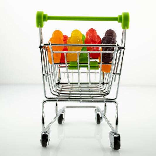 Gone Shopping 2303v1 - Close Detail View, colourful jelly baby figures packed neatly inside a miniature chrome shopping trolley with green handles, staged on a clean white background, fine art photography by Raymond Mather, ART1.