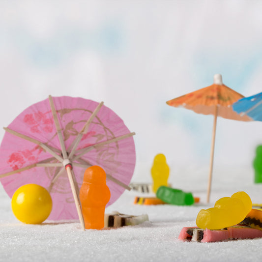 Life’s a Beach 1395 - Close Detail View, colourful jelly baby figures staged on a sugar-sand beach with cocktail umbrellas, licorice towels, and a yellow beach ball, fine art still life by Raymond Mather, ART1.