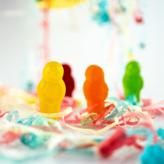 Life’s a Party 2417v2 - Close Detail View, colourful jelly baby figures surrounded by festive paper streamers on a reflective white surface, fine art photograph by Raymond Mather, ART1.