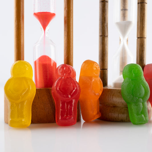 Like Sands Through the Hourglass 2678v1 - Close Detail View, whimsical still life of colourful jelly baby figures standing beside vintage sand timers with red and white sand, reflecting time, nostalgia, and childhood in a playful conceptual fine art photograph by Raymond Mather, ART1.