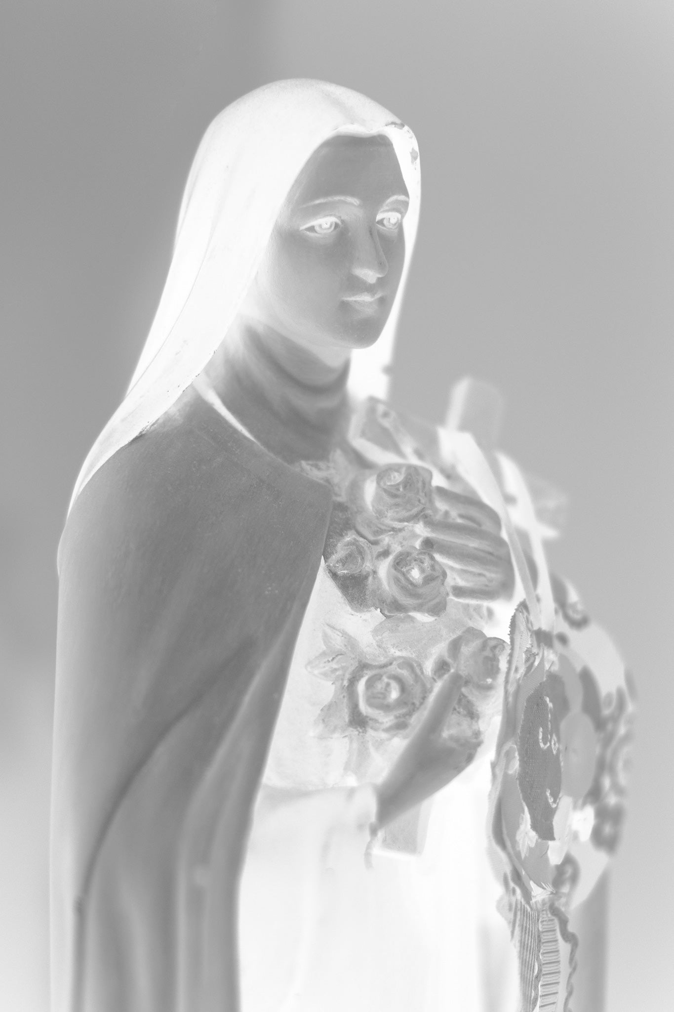 Monochrome Mix - Icons on the Mantel - 183073 - 60x90cm, A soft black and white image of Saint Thérèse of Lisieux holding roses and a cross, exuding peaceful grace and spiritual tenderness.