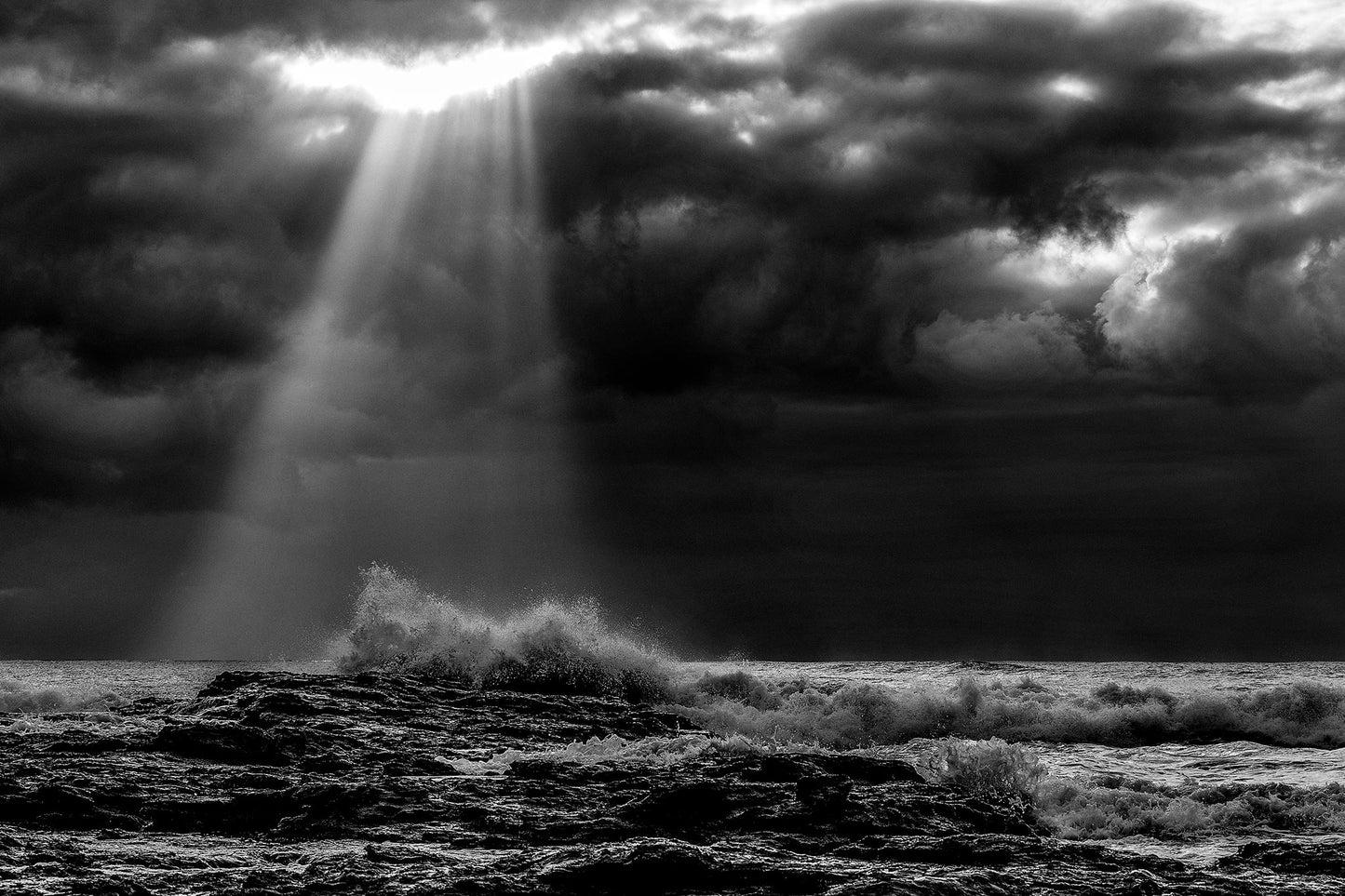 Monochrome Mix - Valla Beach - Cloud Burst - 171683 - 90x60cm, Black and white photograph of stormy ocean waves crashing on rocks beneath dramatic cloud cover, with beams of sunlight piercing through the clouds over Valla Beach.