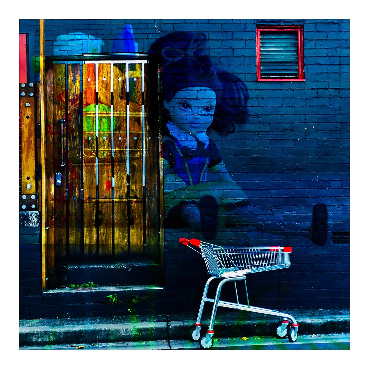 Trolley Dolly - Series No.2: 19E2255v16 - 74x74cm, a dark haired rag doll with outstretched limbs is layered onto a blue brick wall beside a red handled shopping trolley. A glowing wooden door sits to the left, overlaid with fruit textures. The composition explores homelessness, emotional fatigue, and invisibility.