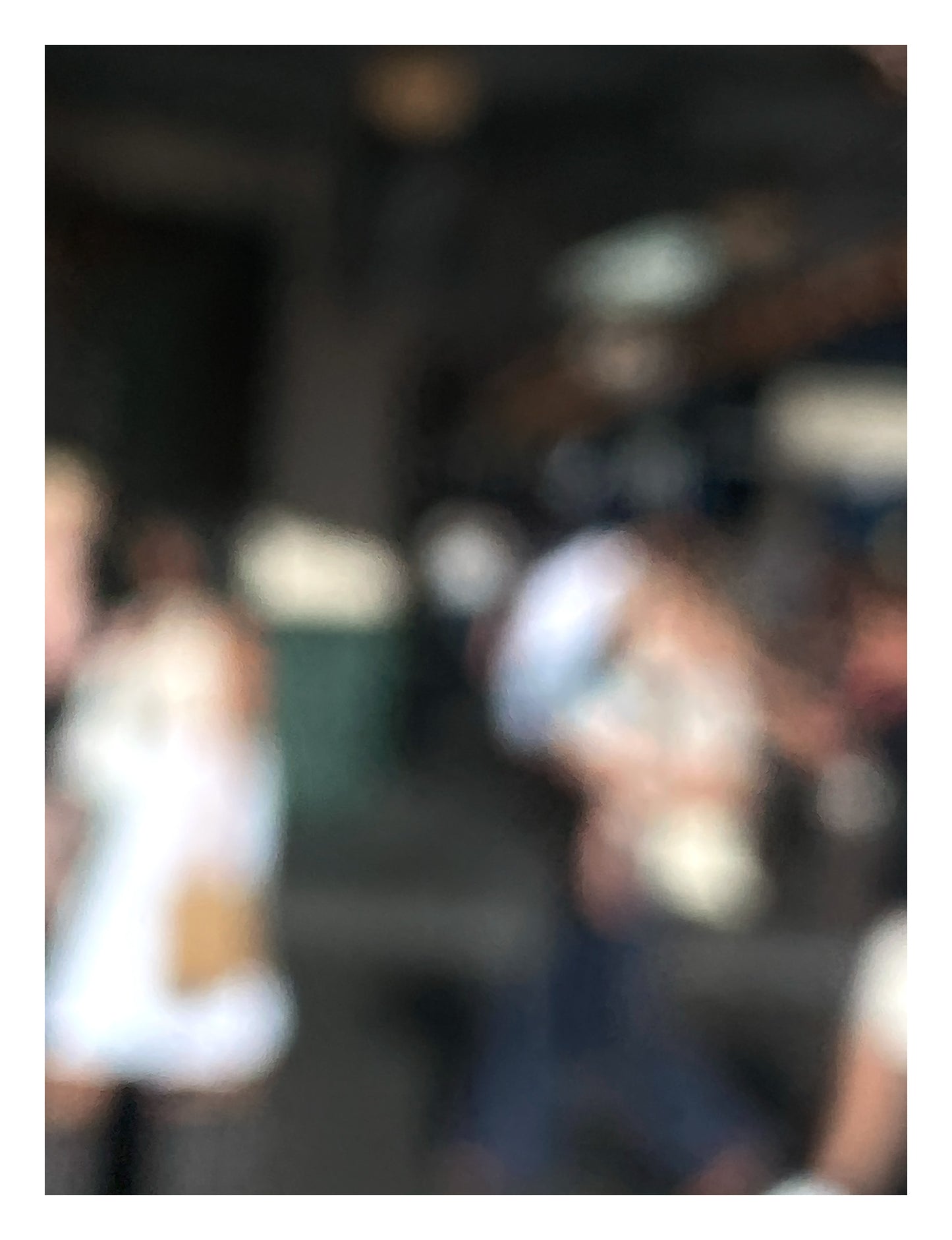 Urban Commute - Series No.1: 0977v1 - 81.5x104cm, a soft focus image of commuters standing and conversing near an entrance or station facade. Blurred outlines suggest movement and pause, with light brushing softly across their forms. A moment of urban rhythm and intimacy. Limited edition fine art print by Raymond Mather.