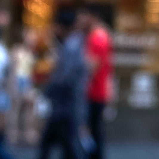 Urban Commute - Series No.1: 0983v1 - Close Detail View, a soft focus photograph of blurred pedestrians in motion, with one figure in bright red passing a golden-lit city storefront. A painterly exploration of rhythm, anonymity, and colour in the urban commute. Limited edition fine art print by Raymond Mather.