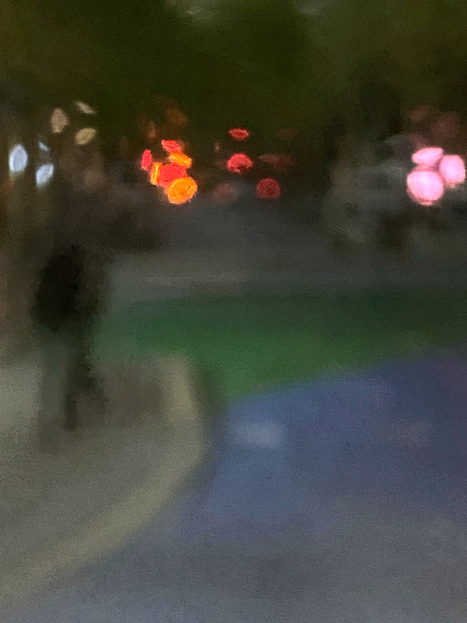 Urban Commute - Series No.1: 1209v1 - 67.5x90cm, a soft focus night scene featuring a solitary walker in a darkened streetscape. Vibrant bokeh lights in red, amber, and pink hover in the distance, surrounded by deep shadow and soft city tones. Limited edition fine art print by Raymond Mather.