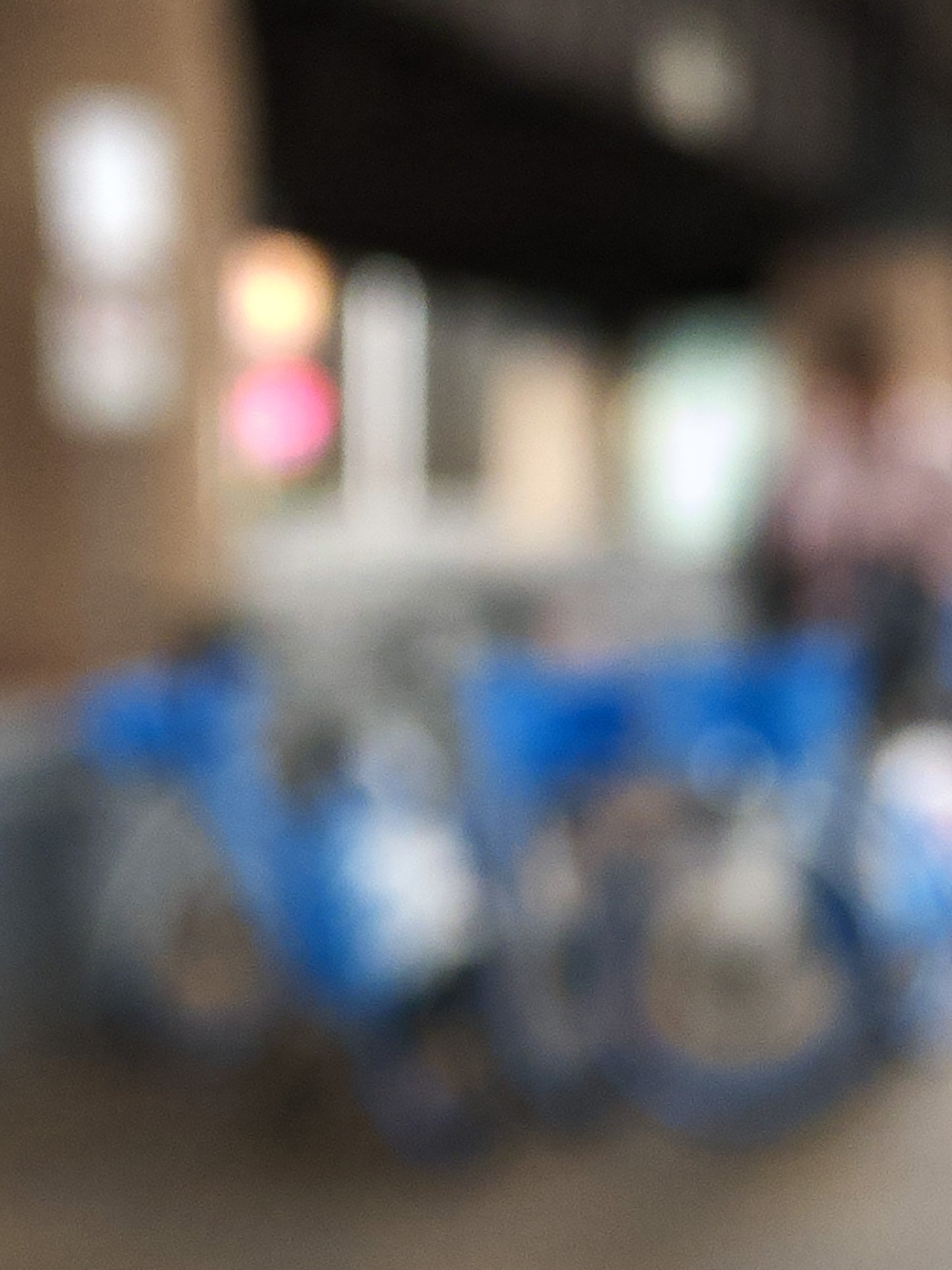 Urban Commute - Series No.1: 9646v1 - 67.5x90cm, a soft focus image of a group of blue city e-bikes parked in a cluster, with blurred lights and architecture in the background. A passing figure adds motion to the scene. Limited edition fine art print by Raymond Mather.